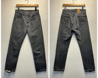 Könnte beinhalten: Eine dunkelgraue Jeanshose mit Knopfleiste und einem kleinen roten Etikett auf der Gesäßtasche.