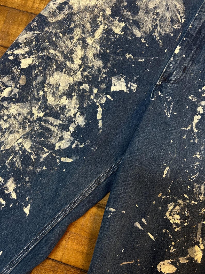 May include: A pair of blue denim jeans with white paint splatters. The jeans have a straight leg and a classic five-pocket design.