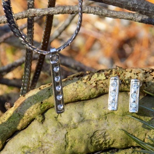May include: A silver necklace with a pendant featuring five clear rhinestones. Matching earrings with three clear rhinestones each are also included.