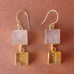 May include: Gold-coloured earrings with a square, pale pink stone at the top and a square, amber-coloured stone at the bottom. The earrings have a simple hook design.