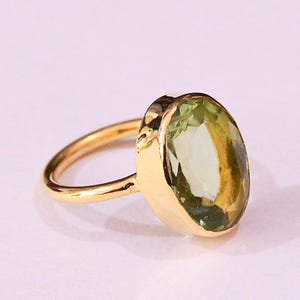 Pode incluir: Um anel de ouro com uma grande gema verde oval. O anel é engastado em uma banda simples.