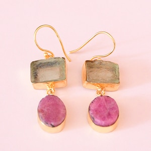 May include: Gold earrings with two-tiered gemstone drops. The top tier is a square-shaped light green stone, and the bottom tier is an oval-shaped pink stone.