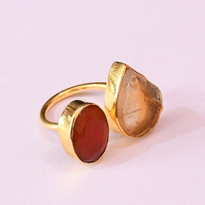 May include: Gold ring featuring two stones. The larger stone is a clear, faceted, teardrop-shaped crystal. The smaller stone is a round, reddish-brown stone.
