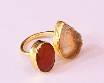 May include: Gold ring with two stones. The larger stone is a clear, faceted, teardrop-shaped crystal. The smaller stone is a round, reddish-brown stone.