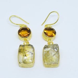 Op de afbeelding: Gouden oorbellen met een traanvormige, heldere kwartsteen en een ronde, amberkleurige steen.