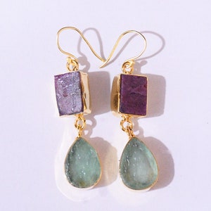 以下が含まれることがあります： 水滴型のアクアマリンと正方形の紫色の石が付いた金のイヤリング