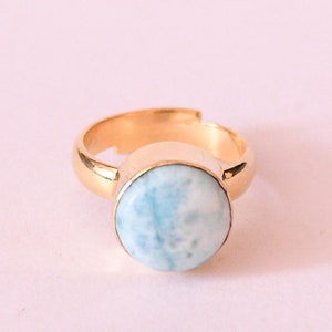 Könnte beinhalten: Ein goldener Ring mit einem runden blauen und weißen Edelstein. Der Ring ist verstellbar und hat ein schlichtes Design.