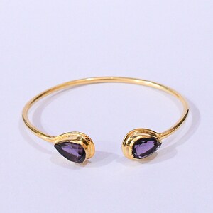 May include: A gold bangle bracelet with two teardrop-shaped amethyst stones.