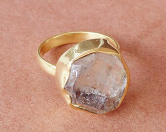 May include: A gold ring with a large, clear quartz crystal set in the center. The crystal is faceted and has a natural, raw look.