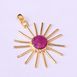 Pode incluir: Pingente dourado com design de sol. O pingente apresenta uma pedra preciosa central, redonda e rosa escuro. Os raios do sol são finos e alongados. A argola é um laço simples para uma corrente.