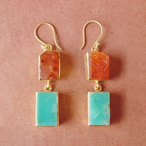 May include: Gold earrings with two teardrop-shaped stones. The top stone is a reddish-orange carnelian and the bottom stone is a light green chrysoprase.