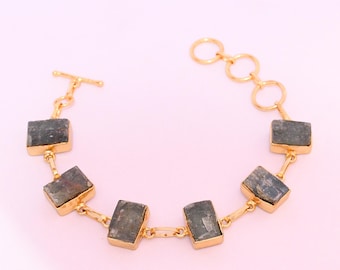 May include: A gold-toned chain bracelet featuring five rectangular, dark grey, textured stone segments set in gold-toned bezels. The bracelet includes a toggle clasp on one end and a series of circular links on the other for adjustable length.