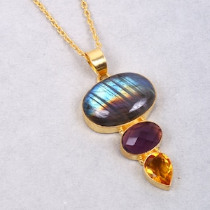 Könnte beinhalten: Eine goldfarbene Halskette mit Anhänger und drei Edelsteinen. Der oberste Stein ist ein ovaler Labradorit mit blau-violettem Schimmer. Darunter befindet sich ein ovaler Amethyst in Lila und unten ein tropfenförmiger Citrin in Gelb.
