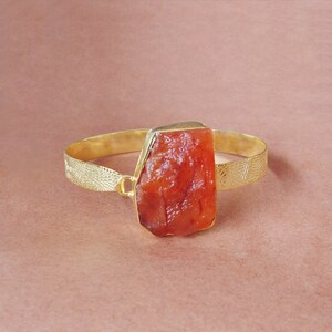 May include: A gold bangle bracelet with a large, irregularly shaped carnelian stone set in the centre.