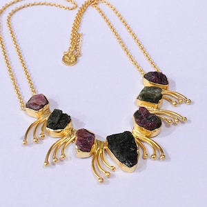 Op de afbeelding: Een gouden ketting met ruwe, ongeslepen groene en roze edelstenen. De stenen zijn gezet in goud en verbonden door een fijne gouden ketting. De ketting heeft een uniek, natuurlijk ontwerp. Kettinglengte ongeveer 40 cm.