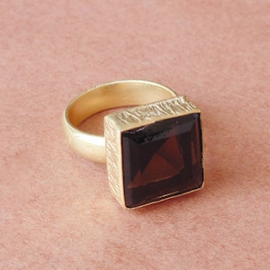 Puede incluir: Un anillo de oro con una gran piedra rectangular de color marrón oscuro.