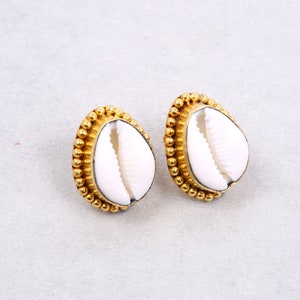 Puede incluir: Un par de pendientes dorados con conchas de cauri blancas. Las conchas están rodeadas por un borde de cuentas.