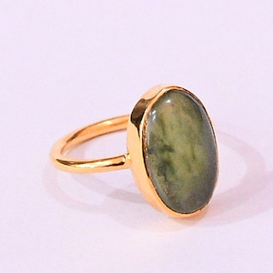 Puede incluir: Un anillo de oro con una gran piedra preciosa ovalada verde. El anillo es simple y elegante.