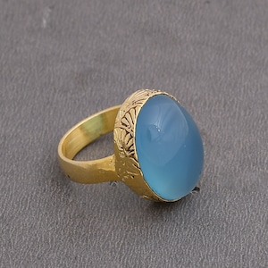 Op de afbeelding: Een gouden ring met een lichtblauwe ovale edelsteen gezet in een decoratieve gouden zetting.