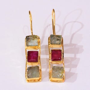 Peut inclure: Paire de boucles d'oreilles dorées, chacune ornée de trois pierres carrées. Les pierres supérieures et inférieures sont vert pâle, tandis que la pierre centrale est rouge foncé. Design simple et élégant.