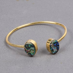 Może przedstawiać: Złota bransoletka z dwoma owalnymi akcentami z muszli abalone. Muszla ma niebieski, zielony i tęczowy kolor.