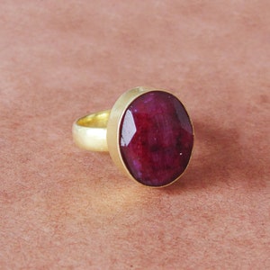 May include: A gold ring with a large, deep red gemstone. The ring is set in a simple, round band.