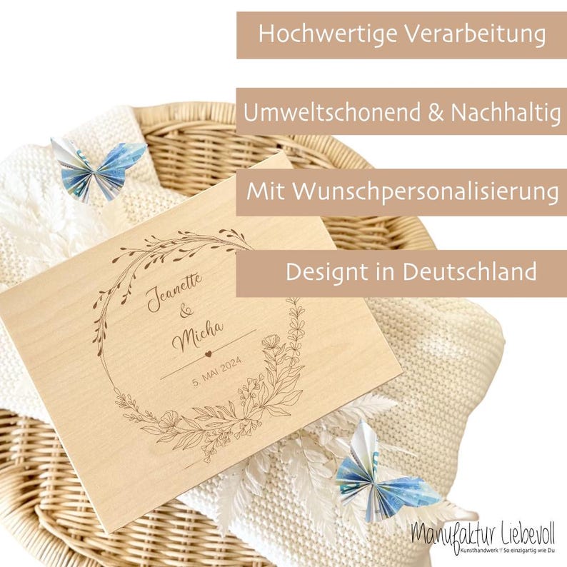May include: A wooden box with a floral design and the text "Jeanette & Micha 5. MAI 2024". The box is sitting on a white blanket and a wicker basket.
