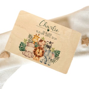 Op de afbeelding: Een houten plaquette met een jungledieren thema. Het staat "Charlie" met een hartje en "10.23 UHR 3210 G 52 CM" in groene tekst. De plaquette toont een giraffe, aap, zebra, nijlpaard, leeuw en olifant.