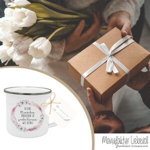 Puede incluir: Taza de esmalte blanco con un dise&ntilde;o floral y el texto "Kleine Menschen brauchen so gro&szlig;e Herzen wie Deins!" Una etiqueta de regalo con la palabra "f&uuml;r" est&aacute; unida a la taza con un cordel.