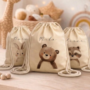 Può includere: Tre sacchetti beige con coulisse con illustrazioni di animali. Una borsa presenta un coniglietto, un'altra un orso e la terza un procione. Ogni borsa ha un nome scritto in corsivo: Nora, Milo e Oliver. Le borse sono in tessuto naturale.