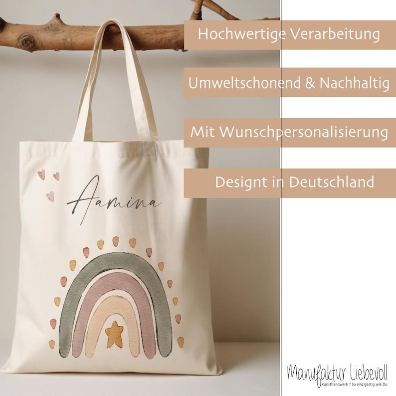 Peut inclure: Un sac fourre-tout en toile blanche avec un motif arc-en-ciel et le nom "Aamina" imprim&eacute; dessus. Le sac a une poign&eacute;e en bois brun et est d&eacute;cor&eacute; de petits c&oelig;urs et de points. Le texte "Hochwertige Verarbeitung", "Umweltschonend & Nachhaltig", "Mit Wunschpersonalisierung", "Designt in Deutschland", et "Manufaktur Liebevoll" est imprim&eacute; sur le c&ocirc;t&eacute; droit du sac.