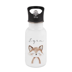 May include: White water bottle with a black lid and a cartoon fox illustration. The fox is brown and white with a smiling face. The name "Ezra" is written above the fox in a cursive font.