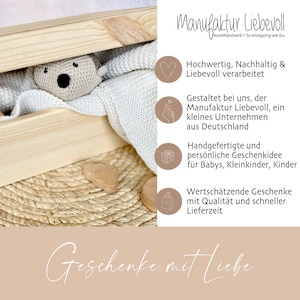May include: A wooden box with a white knitted blanket and a crocheted stuffed animal inside. The box is on a woven mat with a wooden heart and a wooden circle. The text "Manufaktur Liebevoll" is in the upper right corner of the image. The text "Geschenke mit Liebe" is at the bottom of the image.
