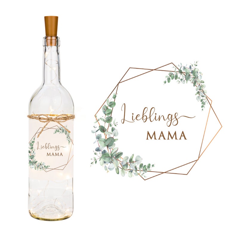 May include: A clear glass bottle with a cork top and a label that says "Lieblings Mama" in a gold geometric frame with eucalyptus leaves.