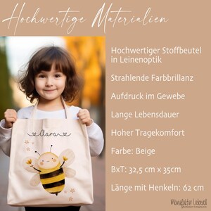 May include: A beige canvas tote bag with a bee illustration and the word "larave" in cursive. The bag has a long handle and measures 12.8 inches by 13.8 inches. The bag is made of high-quality materials and has a long lifespan.