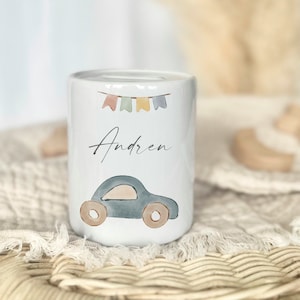 May include: White ceramic piggy bank with a blue car, colorful flags, and the name "Andren" written on it.