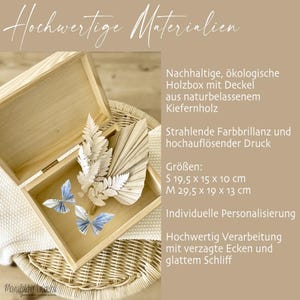 May include: A wooden box with a lid, made from natural pinewood. The box is open and contains a decorative arrangement of dried palm leaves and paper butterflies. The box is available in two sizes: small (19.5 x 15 x 10 cm) and medium (29.5 x 19 x 13 cm). The text "Hochwertige Materialien" is visible at the top of the image.