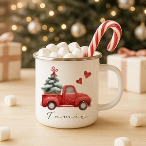 Könnte beinhalten: Ein weißer Emaillebecher gefüllt mit Marshmallows und einem Zuckerstangen. Der Becher zeigt einen roten Truck mit einem Weihnachtsbaum, zwei roten Herzen und dem Namen "Tamie".