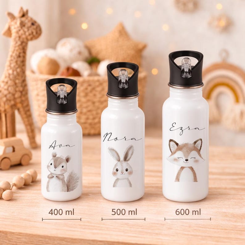 May include: Three white water bottles with black lids, each featuring a different animal illustration and a name: Ava with a squirrel, Nora with a bunny, and Ezra with a fox. Capacities are 400ml, 500ml, and 600ml.