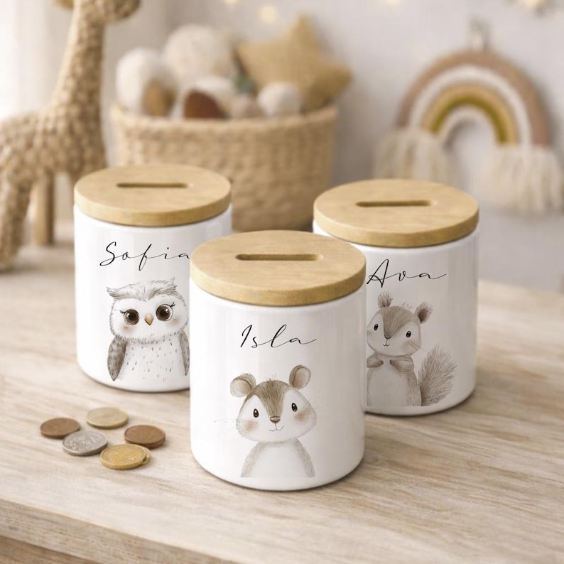 Puede incluir: Tres huchas de cer&aacute;mica blanca con tapas de madera. Cada hucha presenta una ilustraci&oacute;n de un animal del bosque: un b&uacute;ho, un rat&oacute;n y una ardilla. Los nombres "Sofia", "Isla" y "Ava" est&aacute;n escritos en las huchas.