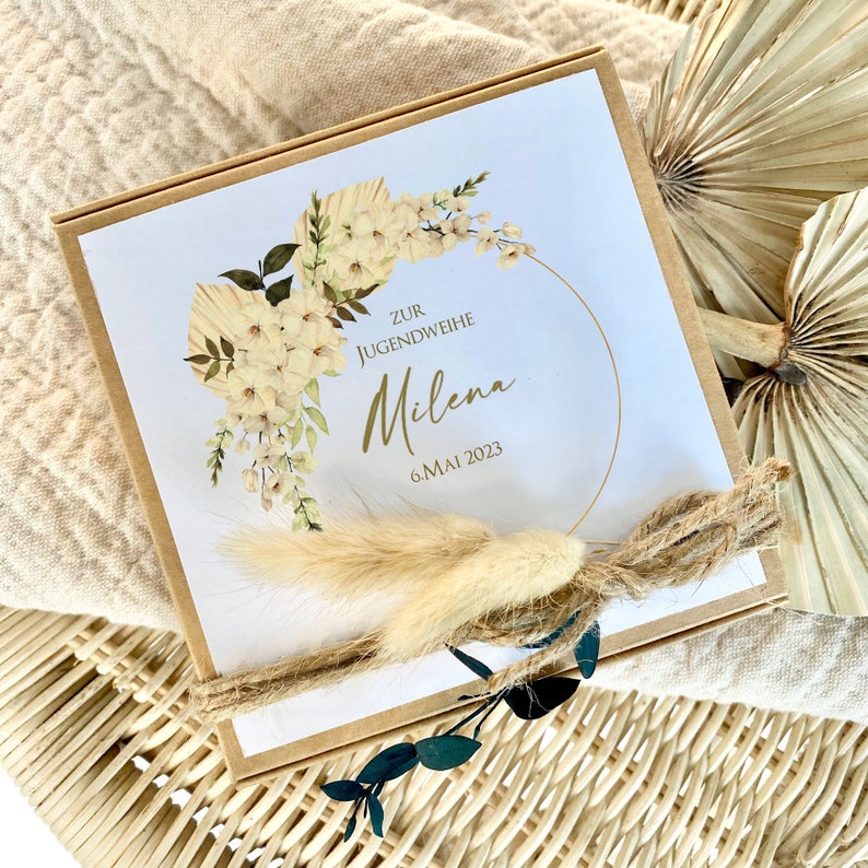 May include: A brown box with a white lid decorated with a floral wreath and the text "Zur Jugendweihe Milena 6. Mai 2023".