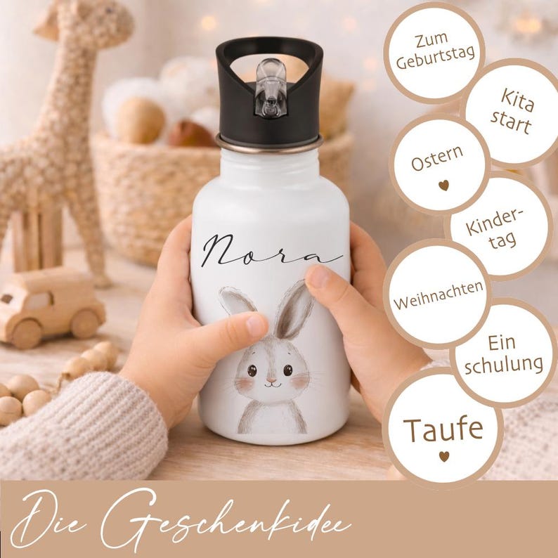 May include: White water bottle with a black lid, featuring a bunny illustration and the name "Nora" in script. The bottle is held by a child. Text on the bottle reads "Die Geschenkidee".