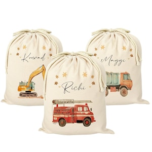 May include: Three personalized gift bags with drawstring closures. Each bag features a different construction vehicle: a yellow excavator, a blue dump truck, and a red fire truck. The bags are made of natural canvas fabric and have a beige background with gold stars and hearts. The names "Konrad", "Maggi", and "Richi" are printed on the bags.