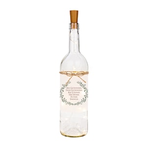 May include: A clear glass bottle with a cork top and a label that reads "Ein Glühwein, Zwei Glühwein, Rei Lühwe, Hie Hühël, Flönël, Snüwln." The bottle is filled with white fairy lights.