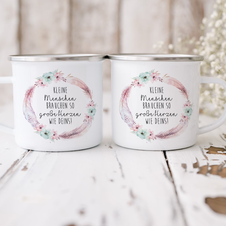 Puede incluir: Dos tazas de esmalte blanco con un dise&ntilde;o floral y el texto "KLEINE Menschen BRAUCHEN SO gro&szlig;e Herzen WIE DEINS!" impreso en ellas.