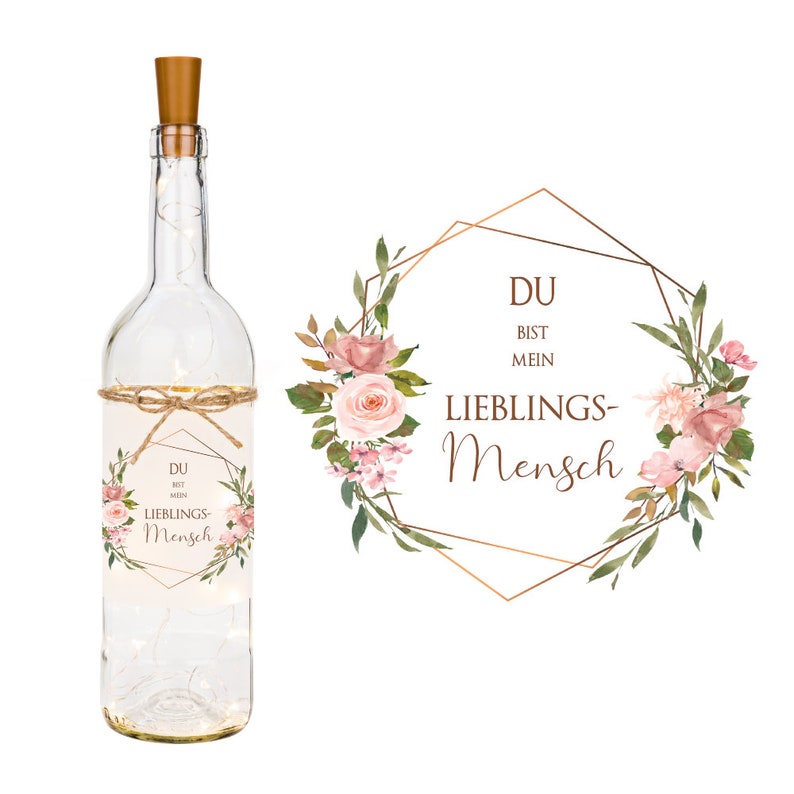 May include: A clear glass bottle with a cork top and a label that says "Du bist mein Lieblings-Mensch". The label is decorated with pink flowers and greenery. The bottle is lit with fairy lights.