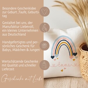 May include: A white pillow with a rainbow design and the name "Emma" written in pink script. The rainbow is made of pink, blue, yellow, and brown stripes. There are pink hearts scattered around the rainbow. The pillow is a personalized gift for a baby.