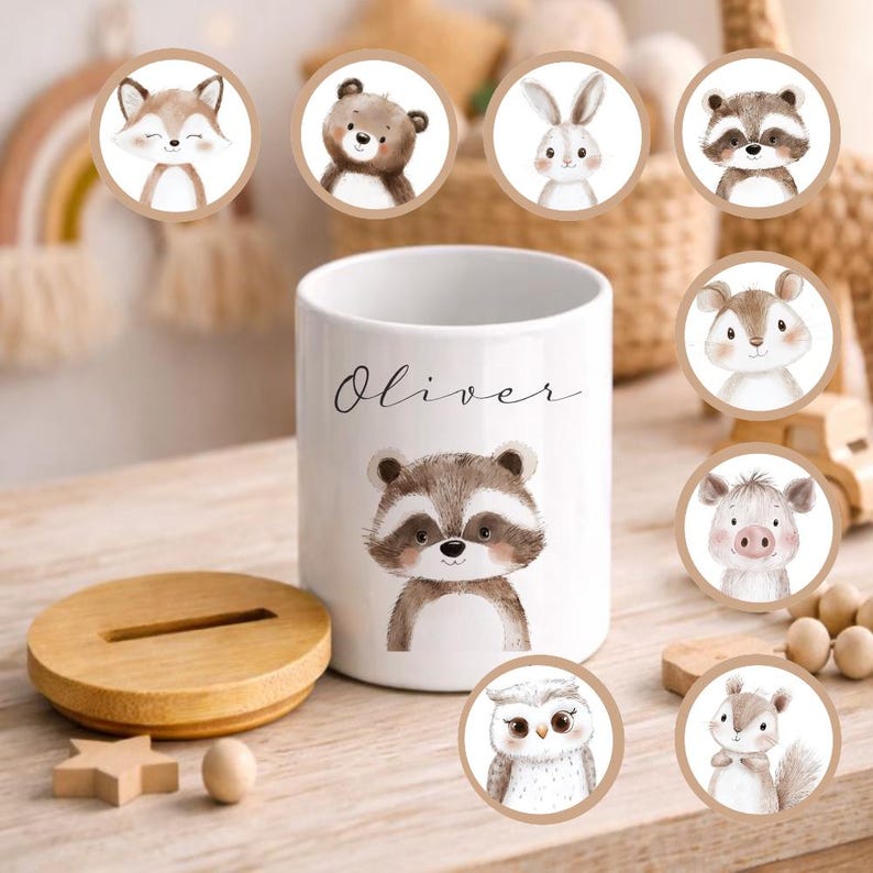 Puede incluir: Contenedor de cer&aacute;mica blanco con una ilustraci&oacute;n de mapache y el nombre "Oliver" en escritura cursiva. Incluye una tapa de madera y varias pegatinas circulares de animales: zorro, oso, conejo, mapache, ardilla, b&uacute;ho y cerdo.