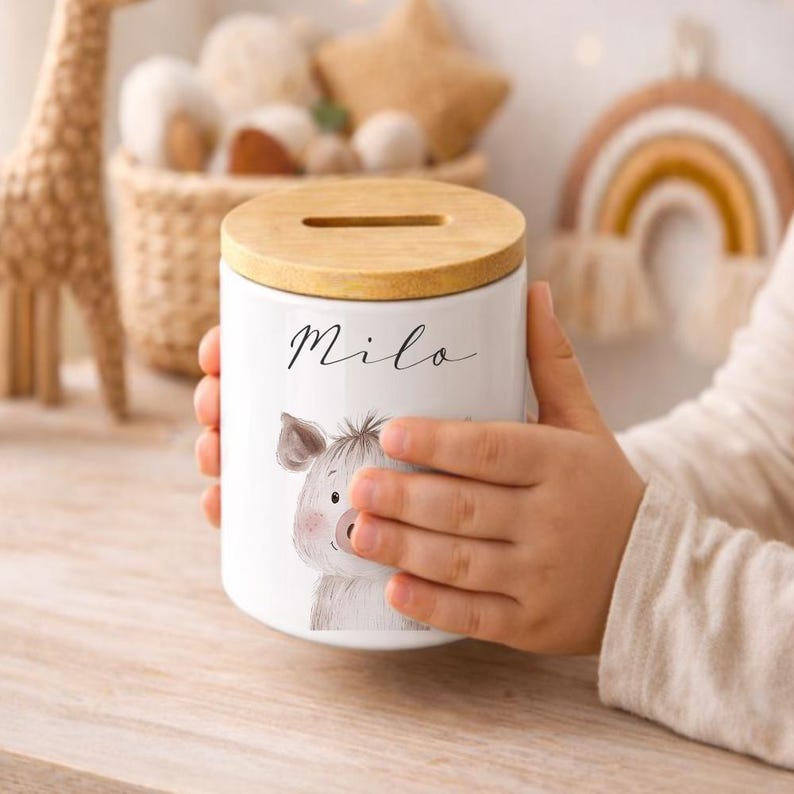 Puede incluir: Hucha de cer&aacute;mica blanca con tapa de madera. La hucha presenta una ilustraci&oacute;n en acuarela de un cerdo y el nombre "Milo" en escritura cursiva. Dise&ntilde;ada para ni&ntilde;os, es un elemento decorativo para una habitaci&oacute;n infantil.