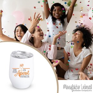 May include: White insulated wine tumbler with a silver lid. The tumbler has the words "Kann Spuren von Aperol enthalten" in orange and brown. The background shows a group of women celebrating with confetti.